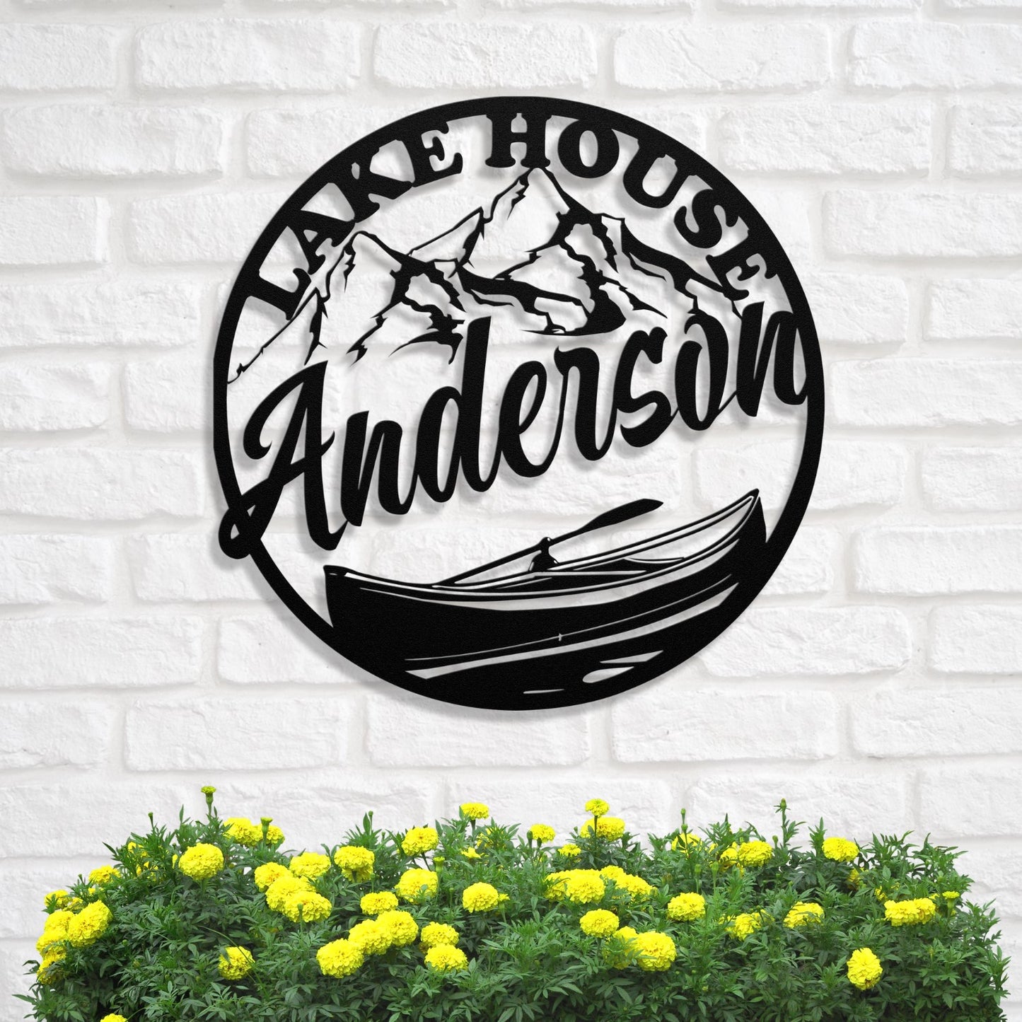 Decorative metal sign with 'Lake House Anderson' text, mountain, and canoe design on a white brick wall.