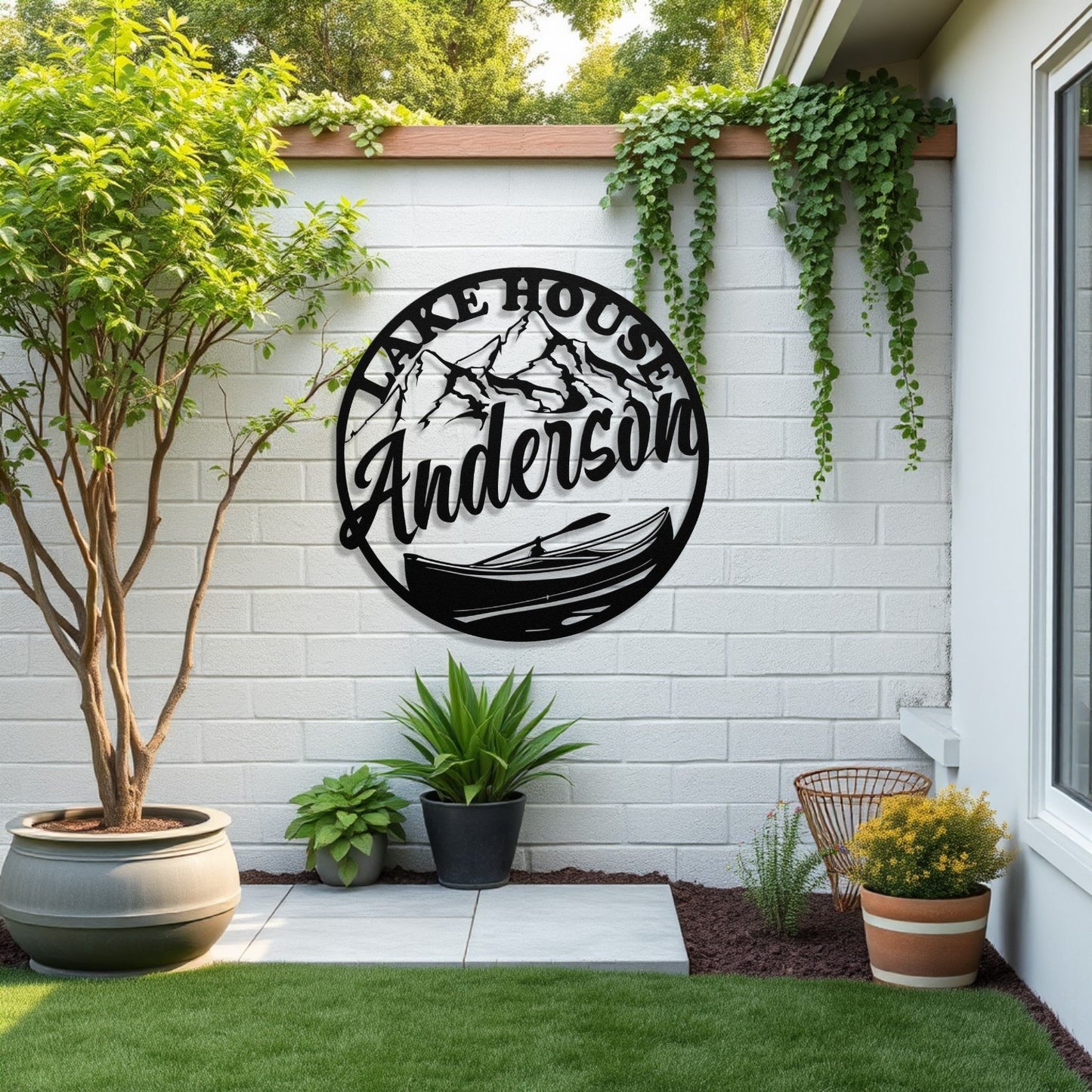 Decorative metal sign with 'Lake House Anderson' on a white brick wall with plants and outdoor furniture.