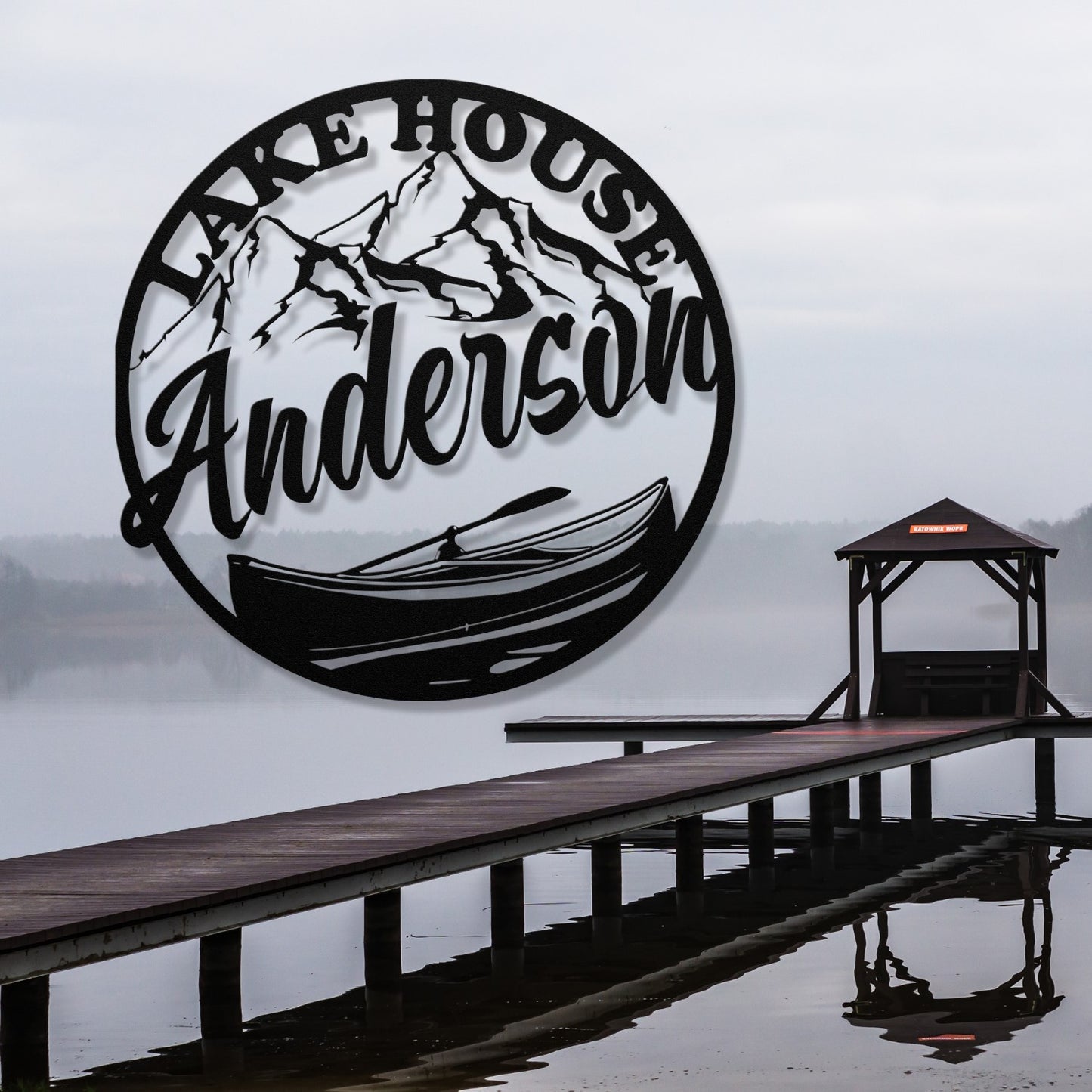 Decorative metal wall art with 'Lake House Anderson' text, mountains, and a canoe design on a white wall.