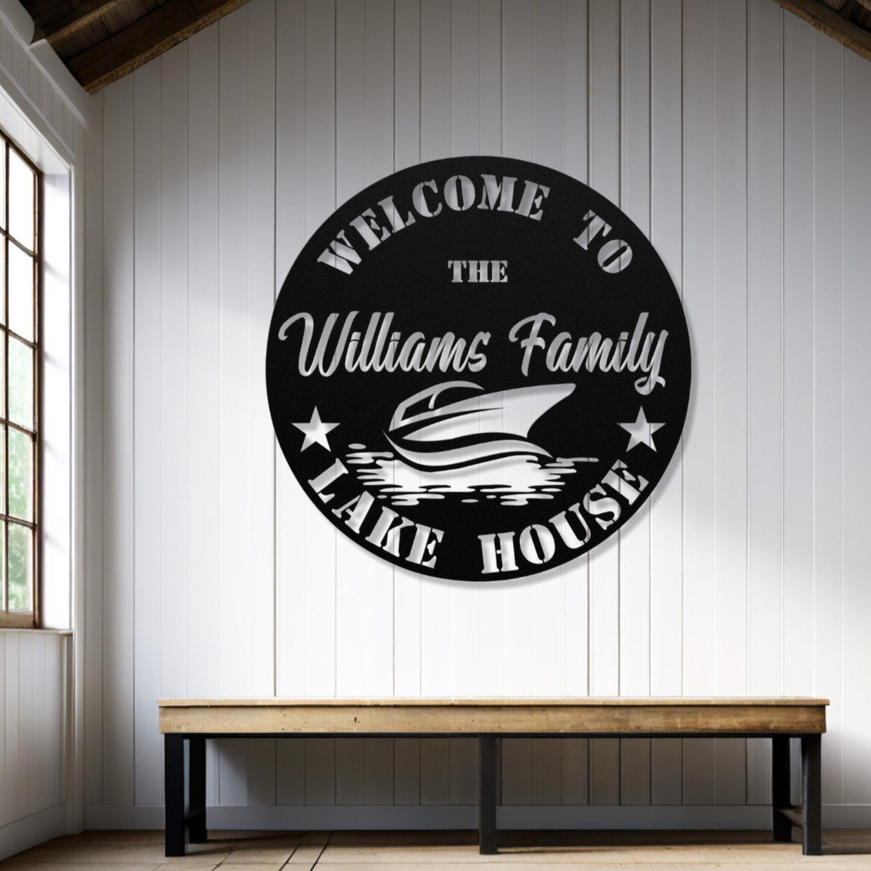Round metal sign with 'Welcome to the Williams Family Lake House' text in a room with wooden floor and window.