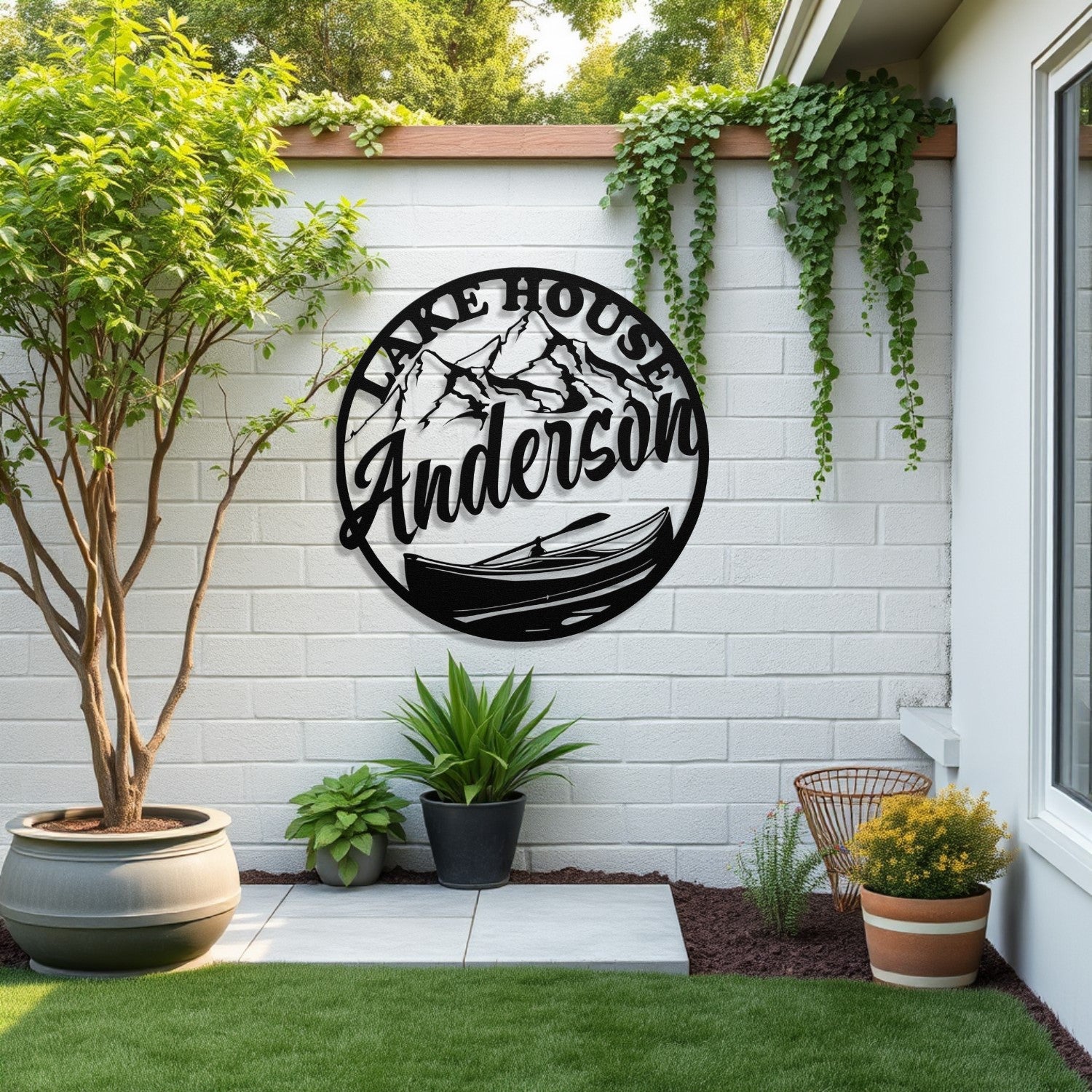 Decorative metal sign with 'Lake House Anderson' on a white brick wall with plants and outdoor furniture.